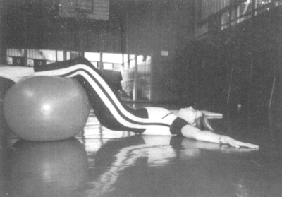 Egy nő gimnasztikai labdán fekszik és edz egy tornateremben.