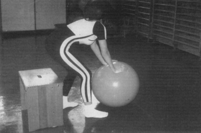 Nő gimnasztikai labdával tornateremben Egy nő edz egy tornateremben, egy nagy gimnasztikai labdát tartva.