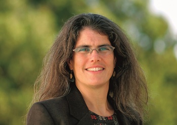 Nő hosszú barna hajjal, fekete zakóban, zöld háttér előtt