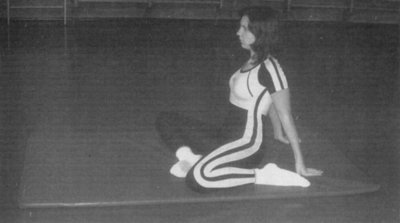 Nő sportos ruhában tornaszőnyegen ülve Nő sportos ruhában tornaszőnyegen ül, hátradőlve támaszkodik a kezére.