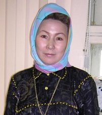 Nő színes fejkendőt visel, sötét mintás ruhában áll.