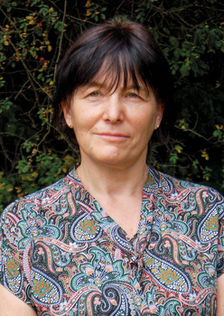 Nő színes mintás ruhában zöld növények előtt Egy nő színes, mintás ruhát visel, háttérben zöld növényekkel.