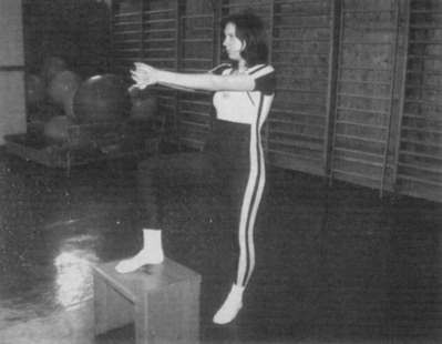 Nő tornagyakorlatot végez tornateremben Nő tornagyakorlatot végez egy tornateremben, egyik lábát emelvényre helyezve, karjait előre nyújtva.