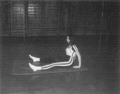 Nő tornateremben sportöltözetben ül a földön Egy nő sportöltözetben ül a földön egy tornateremben, háttérben tornaszerek.