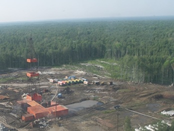 Olajfúró torony erdős területen Olajfúró torony egy erdős területen, körülötte konténerek és munkagépek láthatók.