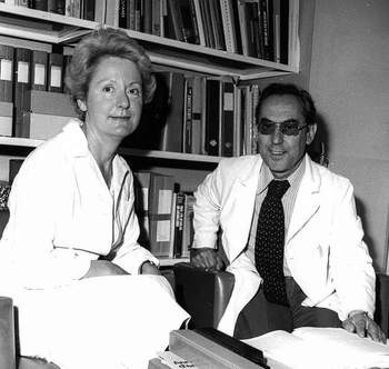 Két orvos fehér köpenyben ül egy könyvtárban, könyvek között.