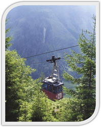 Piros kabinos felvonó halad egy hegyvidéki táj felett, körülötte zöld erdő.