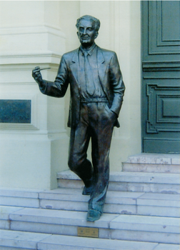 Puskás Tivadar bronz szobra lépcsőn Bronz szobor egy férfiról, Puskás Tivadar, elegáns öltönyben lépdel lefelé egy lépcsőn.