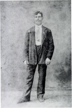 Régi fekete-fehér fotó egy öltönyös férfiról Régi fekete-fehér fotó, amelyen egy férfi áll öltönyben és nyakkendőben.