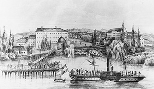 Régi gőzhajó a Dunán, háttérben egy városrészlet, híd és épületek láthatók.