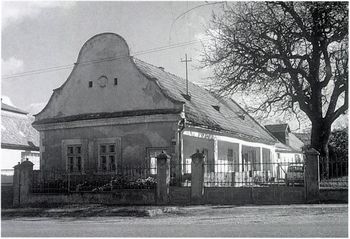 Régi vidéki ház homlokzata és fa Régi, hagyományos stílusú vidéki ház kerítéssel és nagy fával az udvaron.