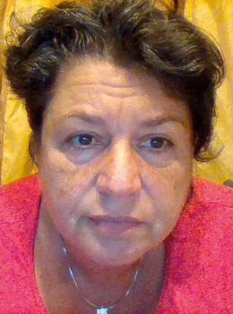 Sötét göndör haj, piros felső és nyaklánc Egy személy sötét göndör hajjal, piros felsőben és nyaklánccal, sárga háttér előtt.