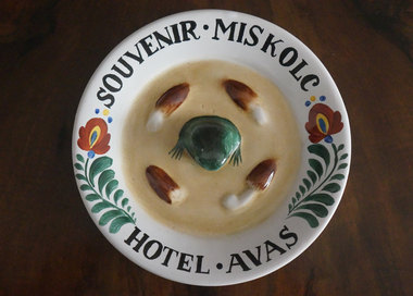 Díszes kerámia tányér, Souvenir Miskolc Hotel Avas felirattal, közepén zöld béka és mandula alakú díszek.