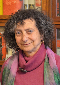 Egy személy bordó garbót és színes sálat visel, a háttérben könyvespolc látható.