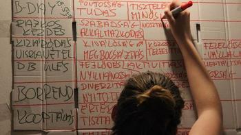 Egy személy kartonlapra ír különböző szavakat piros filctollal, feliratokkal.