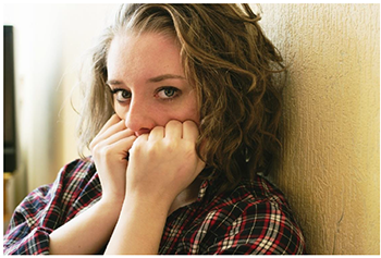 Személy kockás ingben falnak támaszkodva Egy személy kockás ingben falnak támaszkodik, haja hullámos.