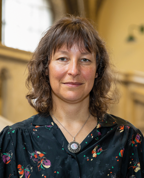 Személy medállal és mintás fekete ruhában Egy személy medállal a nyakában, mintás fekete ruhát viselve.