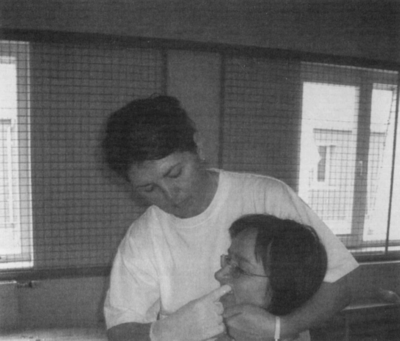 Személy ölelés közben egy rácsos ablak előtt Egy személy ölel át egy másik személyt egy rácsos ablak előtt, beltéri környezetben.