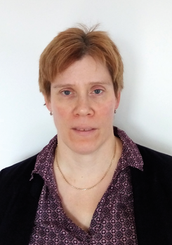 Személy rövid világosbarna hajjal, lila blúzban és fekete zakóban Személy rövid világosbarna hajjal, lila mintás blúzban, fekete zakóban és arany nyaklánccal