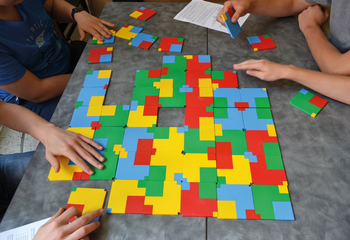 Emberek színes puzzle darabokkal játszanak egy asztalon, kreatív szórakozás.