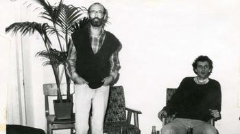 Két ember látható egy szobában, ahol növények és székek vannak.