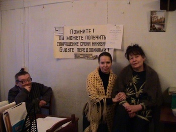 Szoba emberekkel és orosz plakáttal a falon Szoba, ahol három ember ül, a falon orosz nyelvű plakát látható.