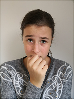 Egy személy szürke, mintás pulóvert visel, keze az arca előtt.