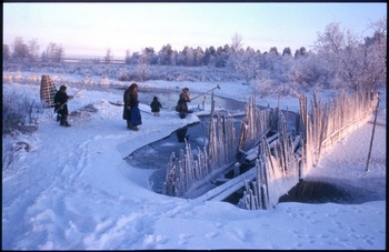 Emberek halásznak egy befagyott folyónál téli tájban, hóval és jéggel körülvéve.