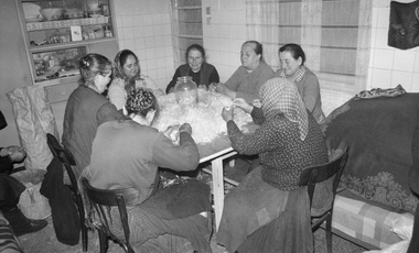 Csoport ember tollfosztást végez egy asztal körül ülve, hagyományos közösségi munka.