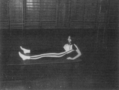 Személy fekvő helyzetben tornateremben Egy személy fekvő helyzetben tornateremben, fehér zokniban és sportnadrágban.