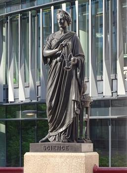 Tudományt jelképező szobor modern épület előtt Szobor, amely a tudományt jelképezi, modern épület előtt, kezében mérleggel, talapzatán 'SCIENCE' felirattal.