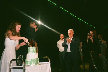 Ünnepi esemény tortavágással Egy nő tortát vág fel egy ünnepi eseményen, körülötte emberek tapsolnak és fényképeznek.