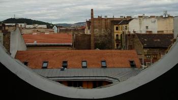 Városi táj kör alakú ablakon keresztül Városi táj, tetők és épületek láthatók egy kör alakú ablak keretében.