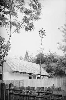 Vidéki ház és templomtorony fák között Vidéki ház fák között, háttérben egy templomtorony látható.