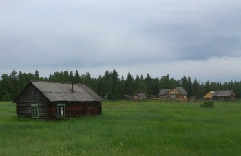 Vidéki táj faépítésű házakkal és zöld mezővel Vidéki táj, ahol több faépítésű ház található egy zöld mezőn, háttérben erdővel.