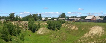 Vidéki táj, fák és dombok, háttérben falusi házak láthatók.